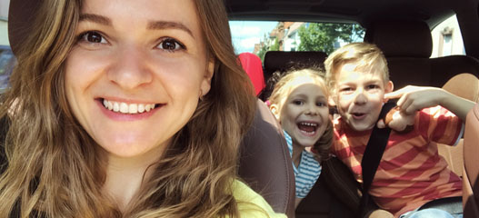 Madre en el coche con hijos detrás haciendo muecas divertidas